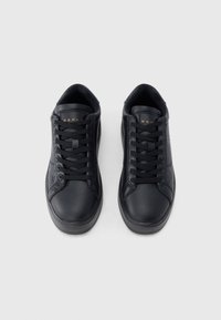 Coppia di sneakers nere basse con motivi in rilievo sui lati e lacci neri, viste dall'alto su sfondo bianco.