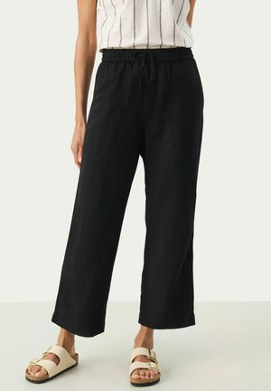 Black, wide-leg trousers made of lightweight fabric with an elastic waistband and side pockets. Paired with light-colored sandals.