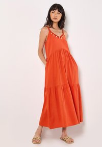 Oranje maxi-jurk met een gelaagd ontwerp, verstelbare spaghettibandjes en decoratieve knopen langs de halslijn. Gemaakt van lichtgewicht stof.