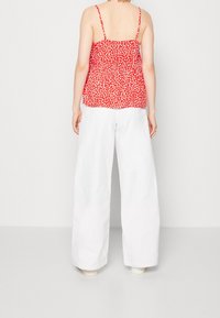 Top sin mangas rojo con puntos blancos y tirantes finos, combinado con pantalones anchos blancos. Ambas prendas cuentan con tejido ligero y un ajuste relajado.