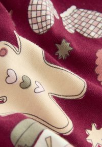 Roter Stoff mit einem wiederholenden Muster aus beige-farbenen Lebkuchenformen, Herzen, Ananassen und Sternen in Pastellfarben. Weiche Textur.