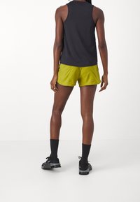 Top negro sin mangas combinado con pantalones cortos de color verde brillante. Los pantalones cortos tienen una textura lisa y un ajuste relajado, complementados con calcetines y zapatos negros.