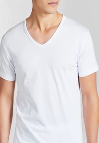 T-shirt bianca a V con collo in morbido cotone, dotata di maniche corte, vestibilità slim e una texture liscia. Design minimalista senza motivi.