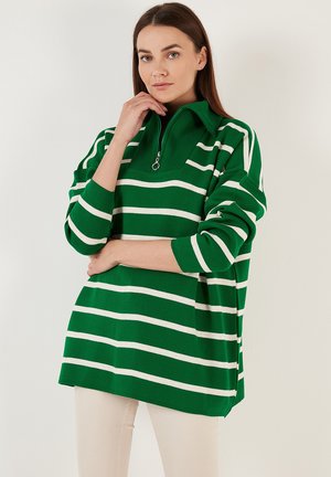 Pull rayé vert et blanc avec un col montant et une fermeture à demi-zippée. Fabriqué en tissu tricoté doux avec des manches longues et une coupe décontractée.