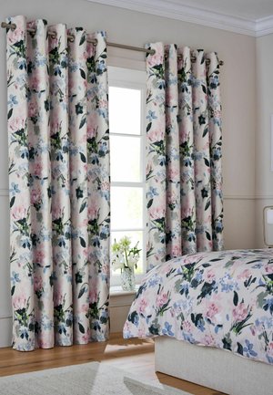 Finestra con tende a motivo floreale abbinate al copriletto in una camera da letto con illuminazione soffusa, pareti beige e pavimento in legno.