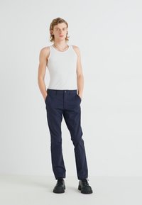Un débardeur blanc à côtes associé à un pantalon bleu marine. Le pantalon est ajusté, avec des poches et une finition lisse. Des bottes à semelle épaisse noires complètent le look.
