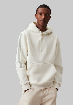 Felpa crema con tasca frontale, cappuccio con lacci e strisce grigie sui maniche. Realizzata in tessuto morbido e confortevole.