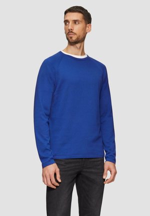 Niebieski sweter z długim rękawem i dekoltem typu crew neck, wykonany z teksturowanej tkaniny. Posiada ribbowane mankiety i dół, zestawiony z ciemnymi dżinsami.