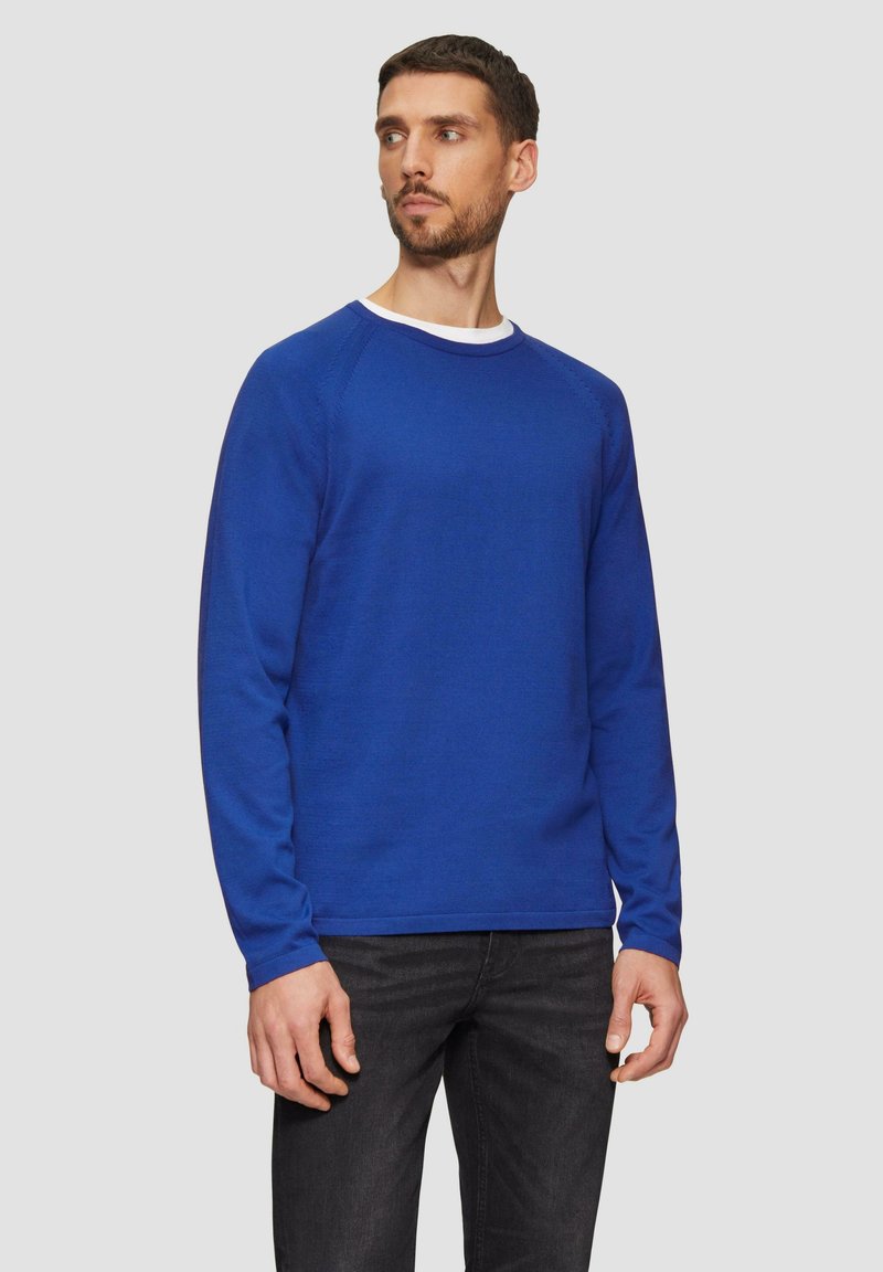 Blauer langärmeliger Pullover mit Rundhalsausschnitt, aus strukturiertem Stoff gefertigt. Mit gerippten Bündchen und Saum, kombiniert mit dunklen Jeans.