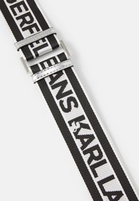 Cintura in tessuto bianco e nero con lettering audace, hardware in argento e design sportivo con una texture intrecciata.