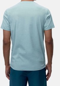 Man med ljusblå kortärmad t-shirt och mörkblå shorts, sedd bakifrån mot en enkel bakgrund.