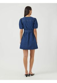 Tummansininen farkkumekko, jossa on valkoisia pilkkuja, puffihihat, muotoiltu vyötärö ja avara helma. Mukana takana vetoketjukiinnitys ja vyö.