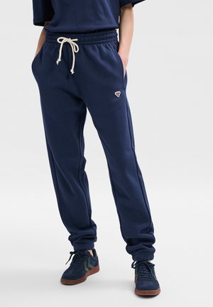 Marina-blå sweatpants med elastiskt midjeband och dragsko, med sidfickor och ribbade muddar. Litet broderat märke framtill.