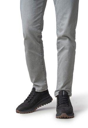 Zwarte sneakers met een gestructureerd bovenwerk, veterontwerp en robuust rubberen zool. Gecombineerd met lichtgrijze, licht aansluitende spijkerbroek.