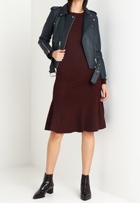 Veste biker en cuir bleu marine portée sur une robe en maille côtelée bordeaux à ourlet évasé, associée à des bottines noires vernies.