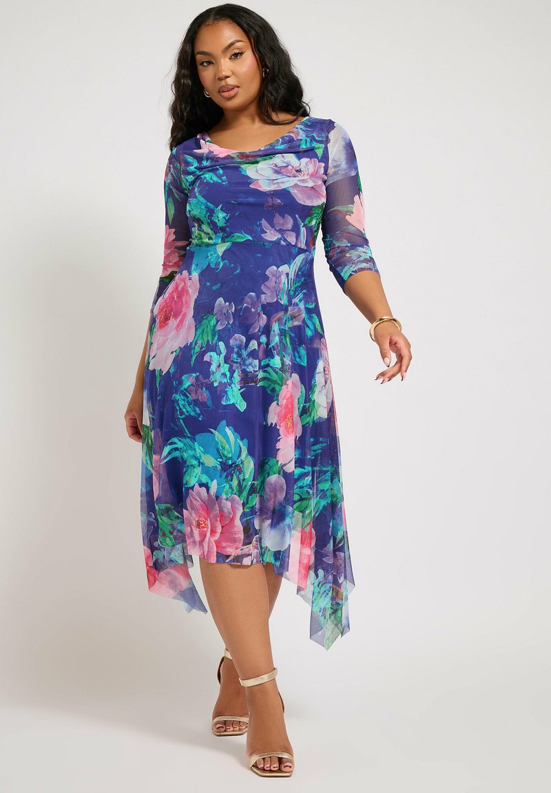 Kukkakuosiset mekko sinivihreällä sävyllä, jossa on kolmannes hihat ja epäsymmetrinen helma. Kangas on läpinäkyvää ja kevyttä.