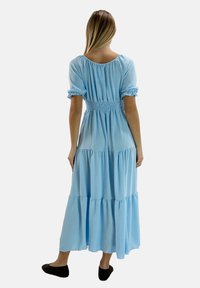 Jasnoniebieska, warstwowa sukienka maxi z marszczonym paskiem w talii, bufkami na rękawach i luźnym krojem. Miękka, fakturowana tkanina. Buty to czarne baleriny.