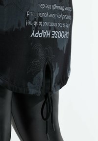 Túnica negra con estampado de tie-dye y gráfico, que cuenta con un dobladillo redondeado, un cordón oculto en la cintura y sutiles detalles florales.