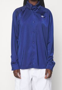 Navy blue long-sleeve shirt made of shiny fabric, featuring a button-up front, a collar, and a small logo on the left chest.
