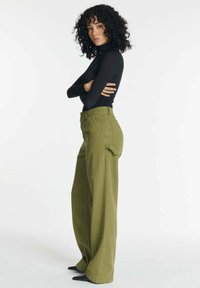 Olijfgroene wijde pijpen broek met frontzakken, hoge taille en lusjes voor een riem. Gepaard met een aansluitend zwart langemouwen top. Soepele textuur.