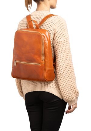 Zaino in pelle tan dalla forma rettangolare, con tasca frontale con zip e spallacci regolabili. Texture liscia con dettagli di cucitura minimi.