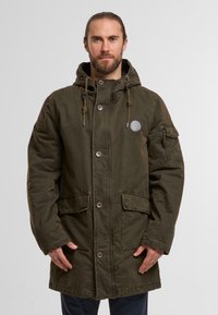 Olivgrüne Parkajacke mit Kapuze, weicher Textur, Knopfleiste, zwei Fronttaschen und einem Patch auf der linken Brust.