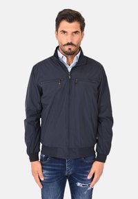 Giacca bomber blu navy con zip frontale, due tasche sul petto, polsini e orlo a coste, e un tessuto liscio e leggero.