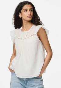 Blusa bianca in cotone con maniche a volants, dettagli in pizzo intricati sulla scollatura, e tessuto leggermente arricciato, abbinata a jeans in denim azzurro chiaro.
