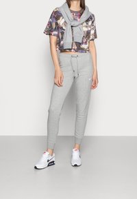 Avskuren blommig t-shirt i lila nyanser, matchad med grå sweatpants med dragsko och logotyp, kompletterad med vita och marinblå sneakers.