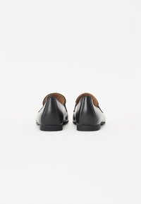 Ballerines en cuir noir avec une finition lisse, bout rond et petit talon. L'intérieur comporte une doublure marron, conçue pour un ajustement serré.