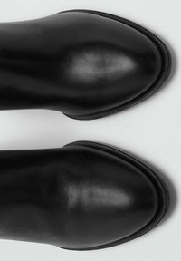 Botas negras de cuero hasta el tobillo con una textura suave, puntera redondeada y un sutil detalle de costura a lo largo del borde. Diseño minimalista sin herrajes visibles.