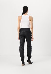 Μαύρο tapered παντελόνι με γυαλιστερή υφή, ελαστική μέση και μανσέτες στον αστράγαλο, σε συνδυασμό με λευκό αμάνικο τοπ και μαύρες γόβες με τακούν�ι.