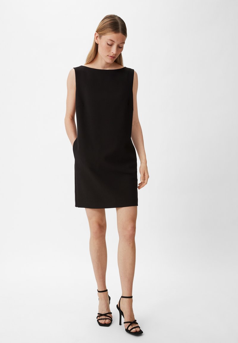 Schwarzes ärmelloses Kleid mit weitem Ausschnitt, zwei seitlichen Taschen und geradem Schnitt, kombiniert mit schwarzen, römischen High Heels.