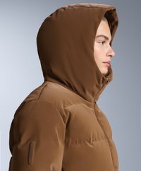 Smeđi izolirani pufast kaput s velikim kapuljačom, koja ima elegantnu, glatku tkaninu i suptilan Recco logo na rukavu.