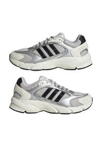 Zapatillas deportivas con una parte superior de malla plateada, rayas negras y acentos blancos. Tienen una suela acolchada y detalles texturizados en los lados.