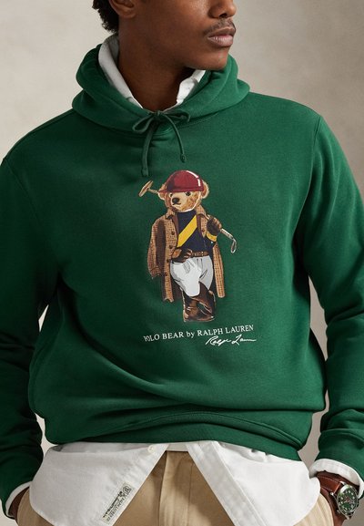 Zeleni hoodić s grafikonom medvjeda u golf odjeći, uz tekst "POLO BEAR by RALPH LAUREN", obučen preko košulje s ovratnikom.