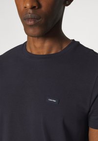 Mornarskoplana pamučna majica s okruglim izrezom i kratkim rukavima, s malim logotipom Calvin Klein na lijevoj strani.