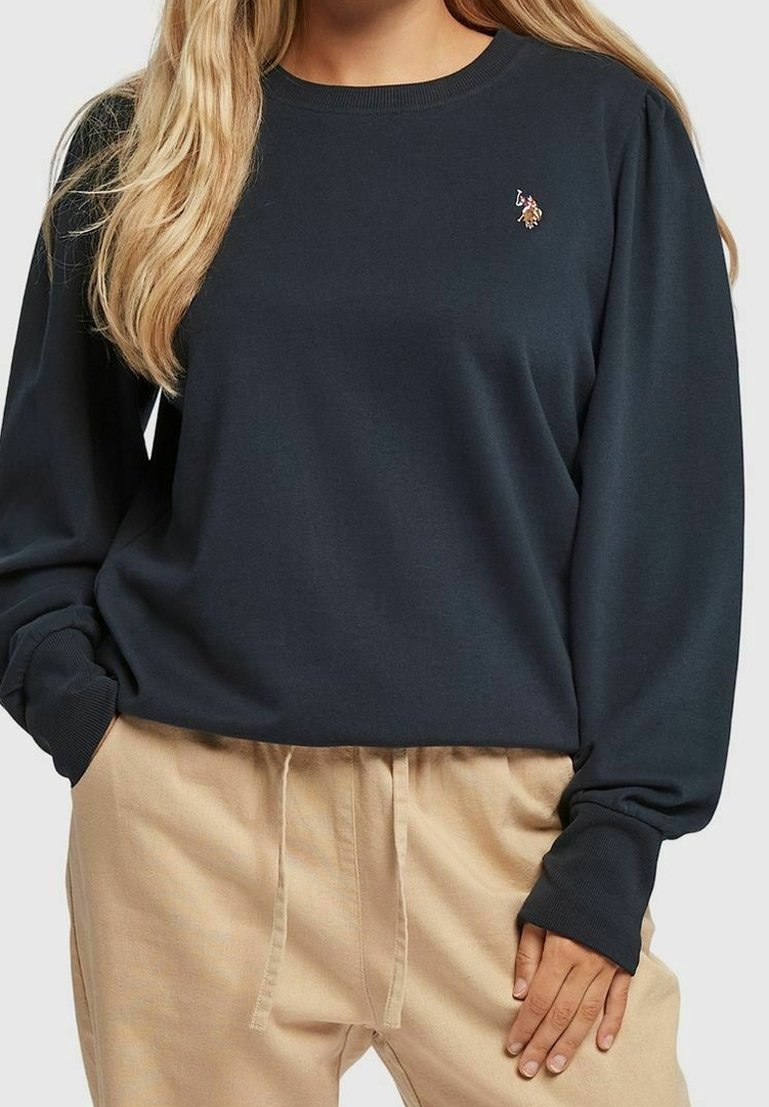 Sweat-shirt bleu foncé à col rond et manches longues ; présente un petit détail graphique sur la poitrine ; associé à un pantalon beige clair.