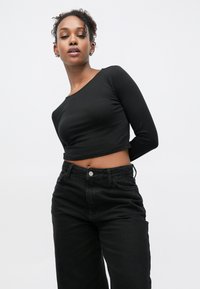 Svart croppet langermet topp kombinert med høytlivs svarte jeans. Toppen har rund hals og tettsittende design, med glatt stofftekstur.