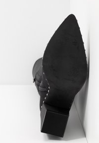 Schwarze Stiefel mit Absatz, quadratischem Absatz, strukturiertem Material, dekorativen Nieten entlang der Kante und geprägten Blumenmustern auf der Sohle.