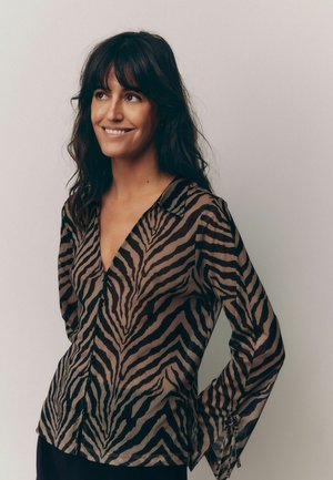 Blouse transparente marron avec des rayures noires en forme de tigre, dotée d'un décolleté en V, de manches longues et de fermetures à boutons sur le devant. Texture lisse.