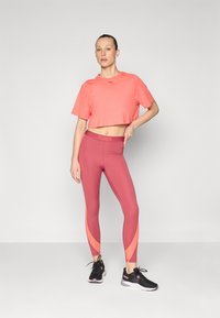 Rosa kortärmad t-shirt med logotyp, ihop med röda leggings med orangea sidopaneler. Svarta träningsskor med rosa detaljer.