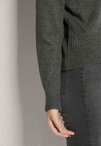 Dunkelgrüner Strickpullover mit gerippten Bündchen, runder Ausschnitt und lässiger Passform, kombiniert mit dunkelgrauen Jeans.