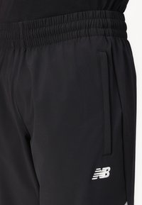Sorte sportsshorts lavet af vævet stof, med elastisk talje, sidelommer og et hvidt "NB" logo på nederste venstre ben.