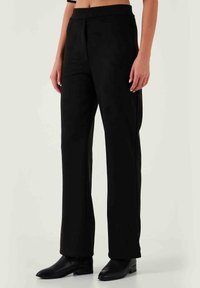 Schwarze weit geschnittene Hosen aus glattem Stoff, mit hoher Taille und einer schlichten vorderen Naht, kombiniert mit eleganten schwarzen Stiefeletten.