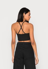Top cropped preto com textura canelada e alças cruzadas estreitas nas costas, combinado com calças pretas de cintura alta com bolsos traseiros.