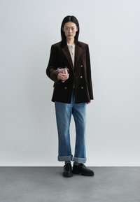 Brown velvet double-breasted blazer over a beige top, paired with loose blue jeans. Black chunky-soled shoes and a small pink bag.