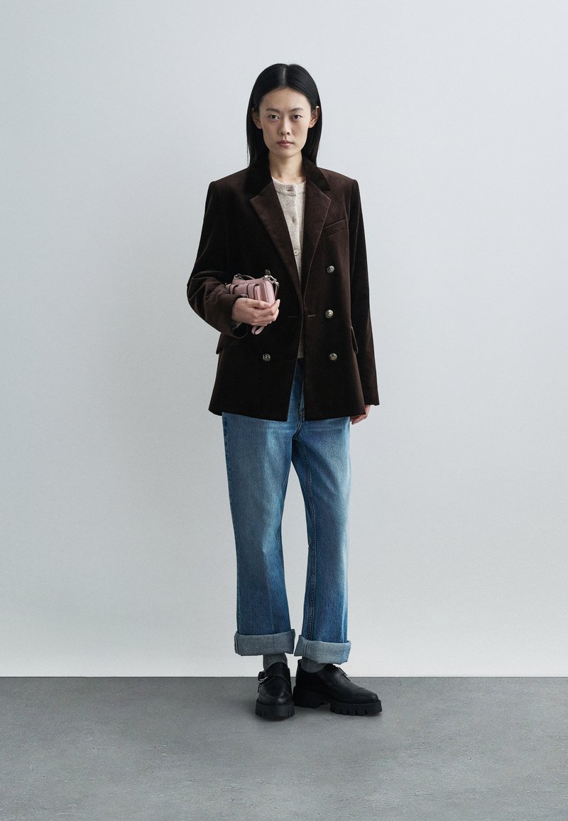 Brown velvet double-breasted blazer over a beige top, paired with loose blue jeans. Black chunky-soled shoes and a small pink bag.