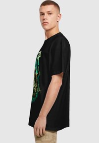 Sort bomulds T-shirt med rund hals, prydet med et levende, detaljeret grafisk design i grøn, der viser et kranietema på forsiden.