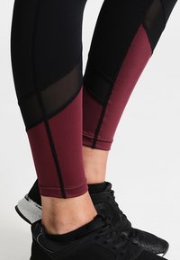 Leggings neri e borgogna con accenti in rete, caratterizzati da un design aderente, una texture liscia e cuciture a contrasto.